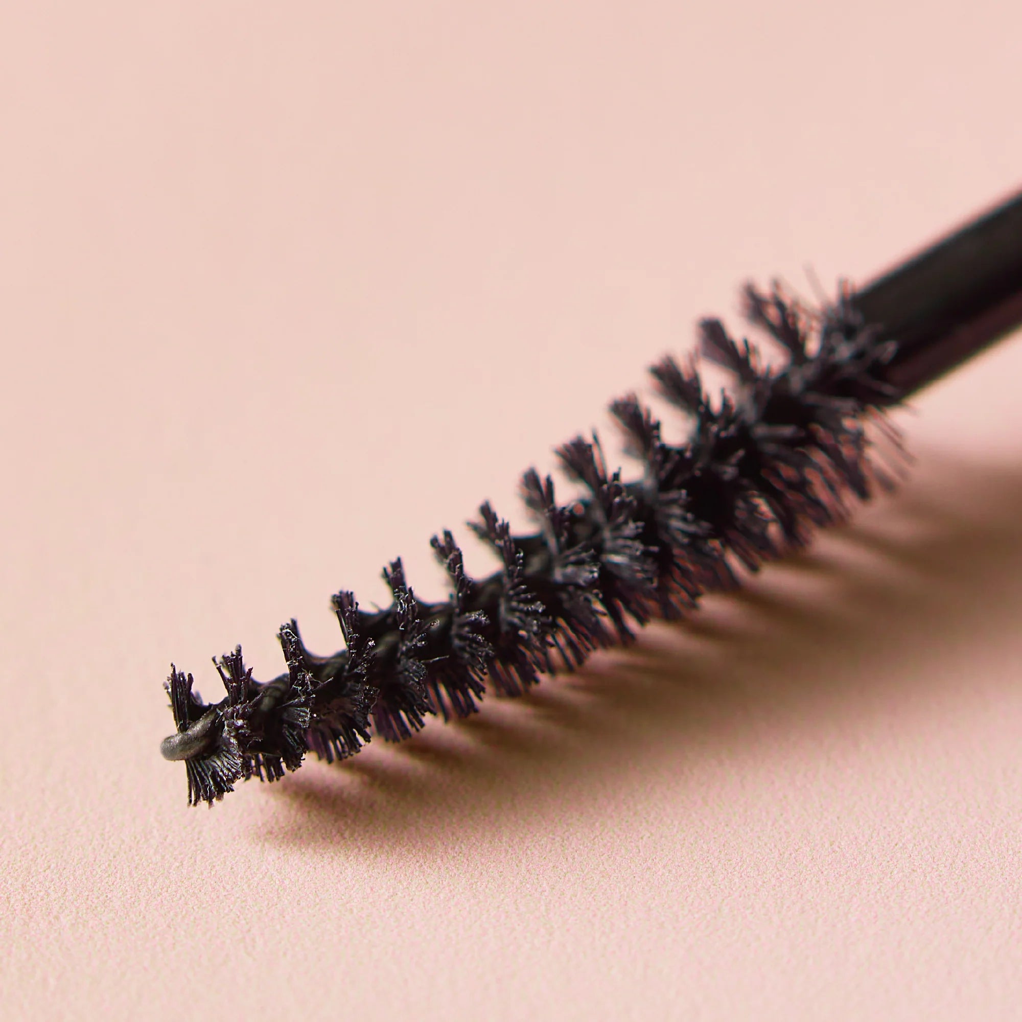 Mascara wand with black bristles on a pink background