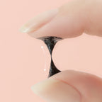 Close-up of a hand holding a black ring with a pink background