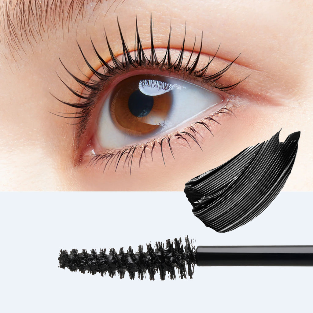 Close-up of a human eye with long, dark eyelashes, shown above a black mascara wand and a thick smear of black mascara on a light gray background.